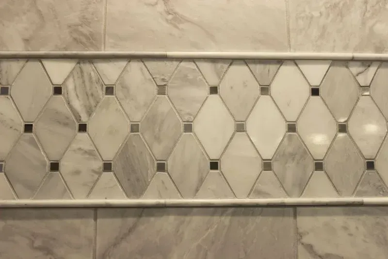 Beige decorative tile wall with diamond and square patterns above a marble baseboard In Bucks County PA