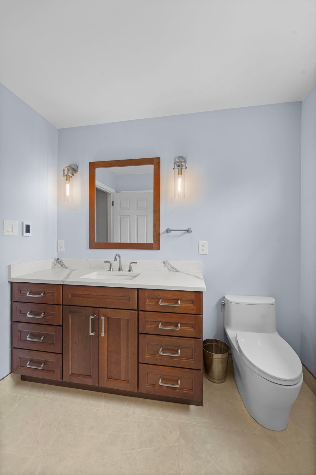 Bathroom vanity with wood cabinets, mirror, sconces, and a toilet on a light blue wall  In Bucks County PA