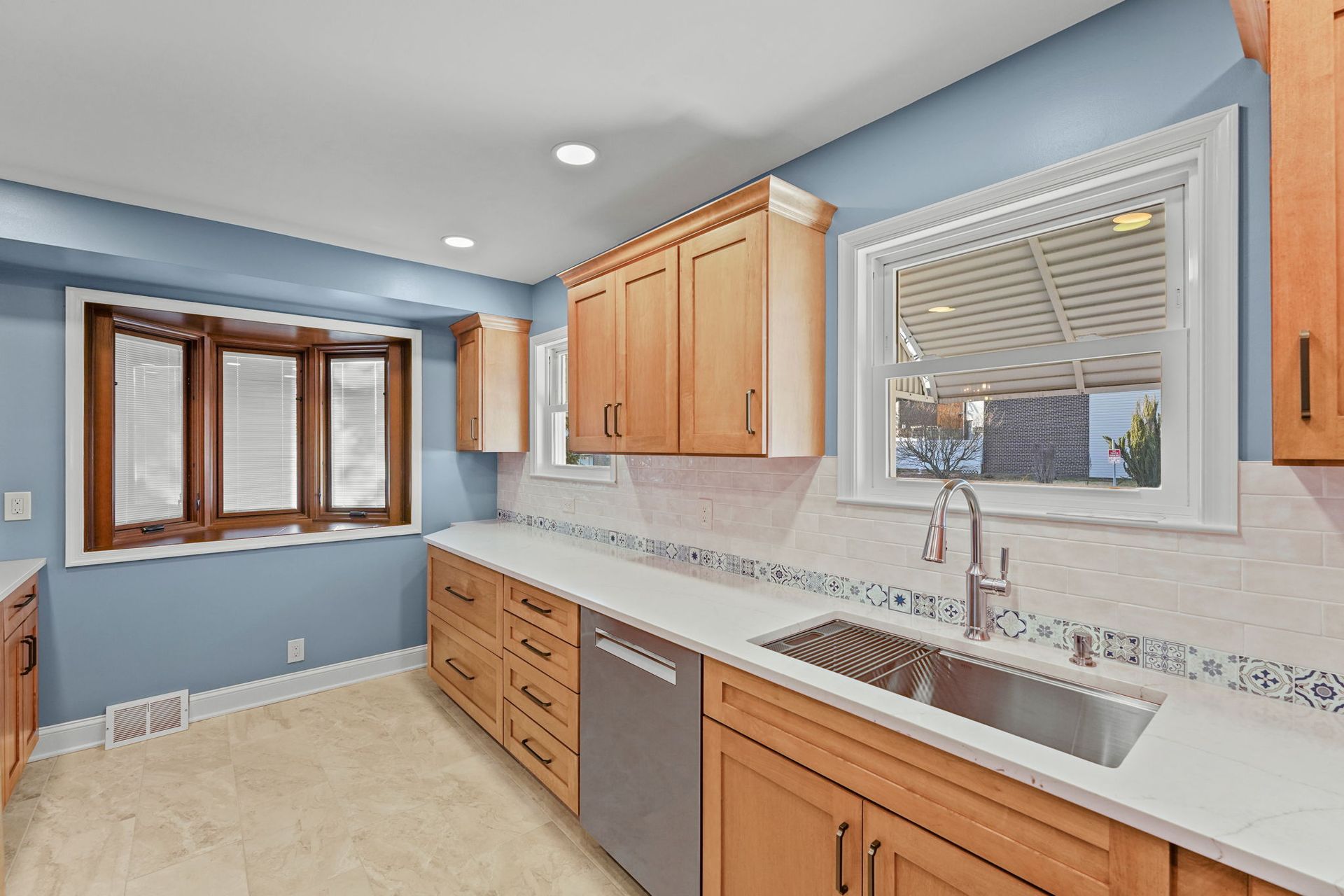 Bright kitchen with wood cabinets, light blue walls, white countertops, and a large window above the sink In Bucks County PA