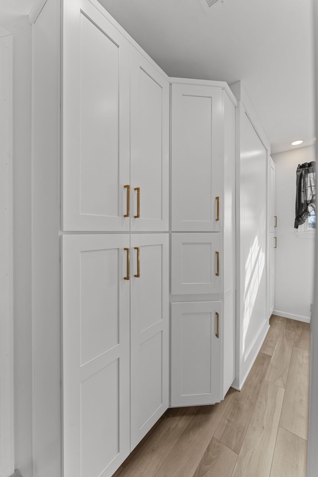 Bright hallway with white built-in cabinets, gold handles, and light wood flooring In Bucks County PA