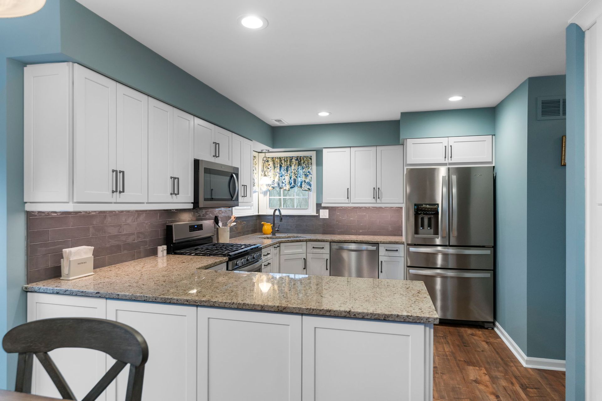 Bright modern kitchen with white cabinets, granite island, stainless appliances, and teal walls In Bucks Country PA
