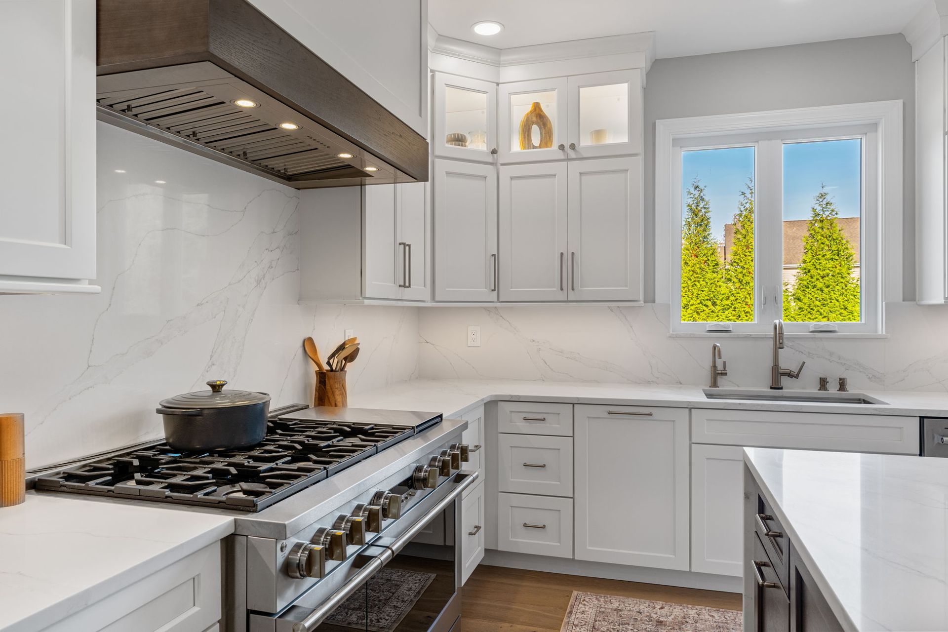 Bright white kitchen with stainless stove, gray cabinets, and a window above the sink showing green trees In Bucks Country PA