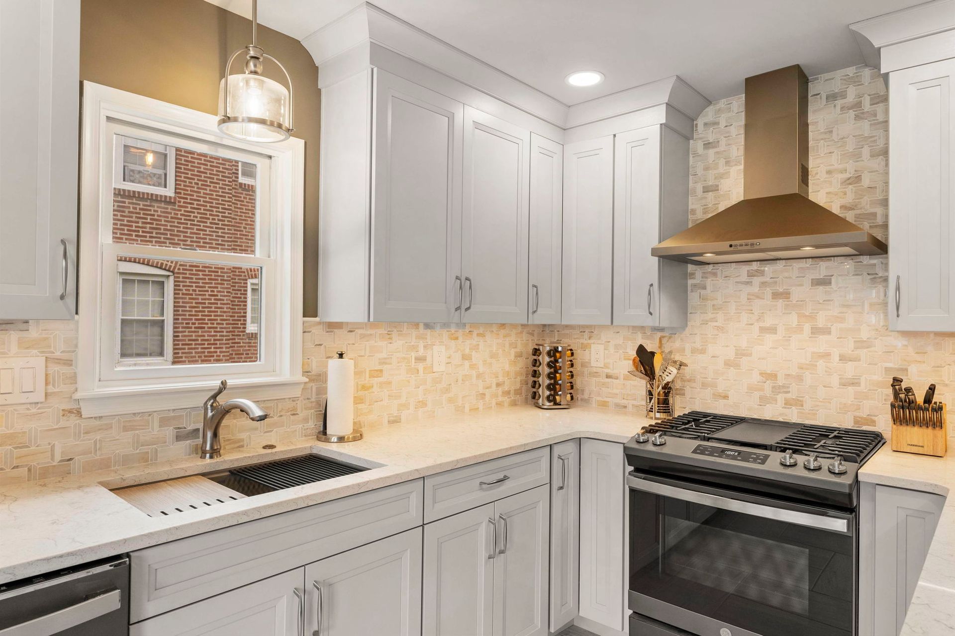 Bright modern kitchen with white cabinets, marble counters, and stainless steel stove and hood In Bucks County PA