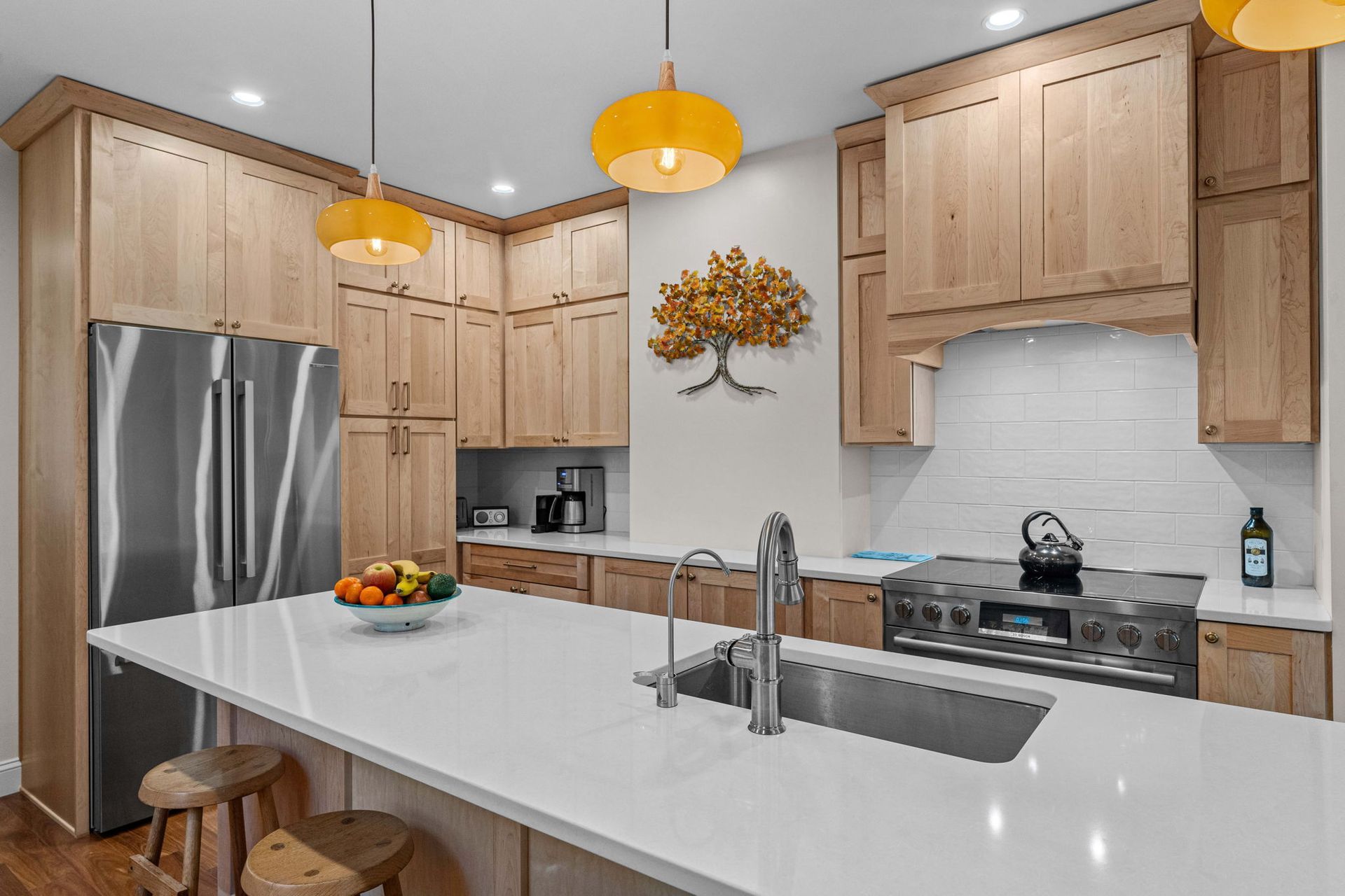 Modern kitchen with light wood cabinets, white island, stainless appliances, and yellow pendant lights In Bucks County PA