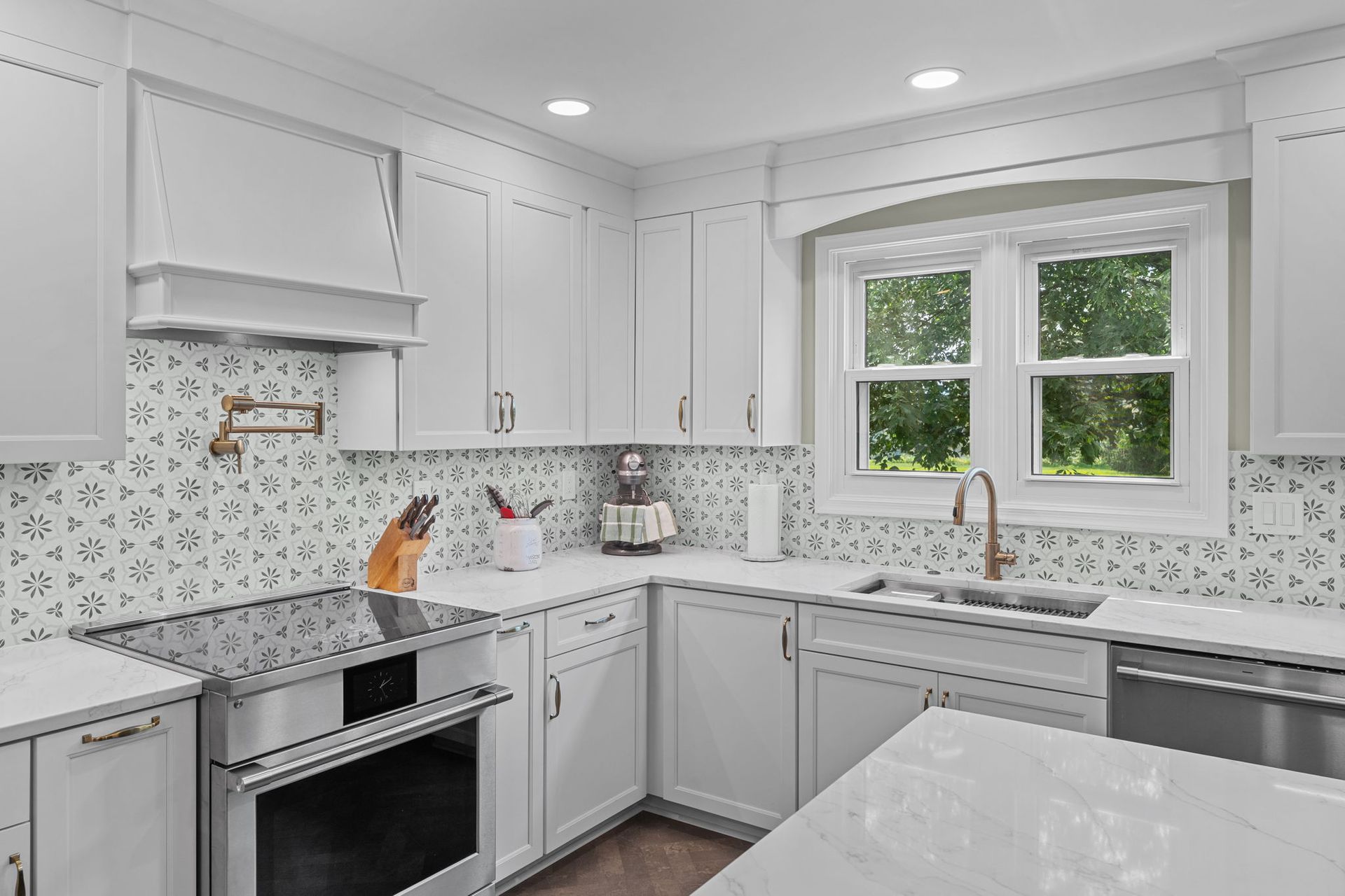 Bright white modern kitchen with marble counters, gray tile backsplash, and a window over the sink In Bucks County PA
