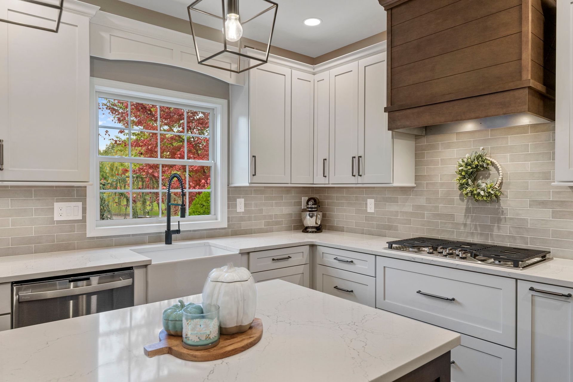 Bright modern kitchen with white cabinets, marble island, stainless sink, and window with autumn trees outside  In Bucks County PA