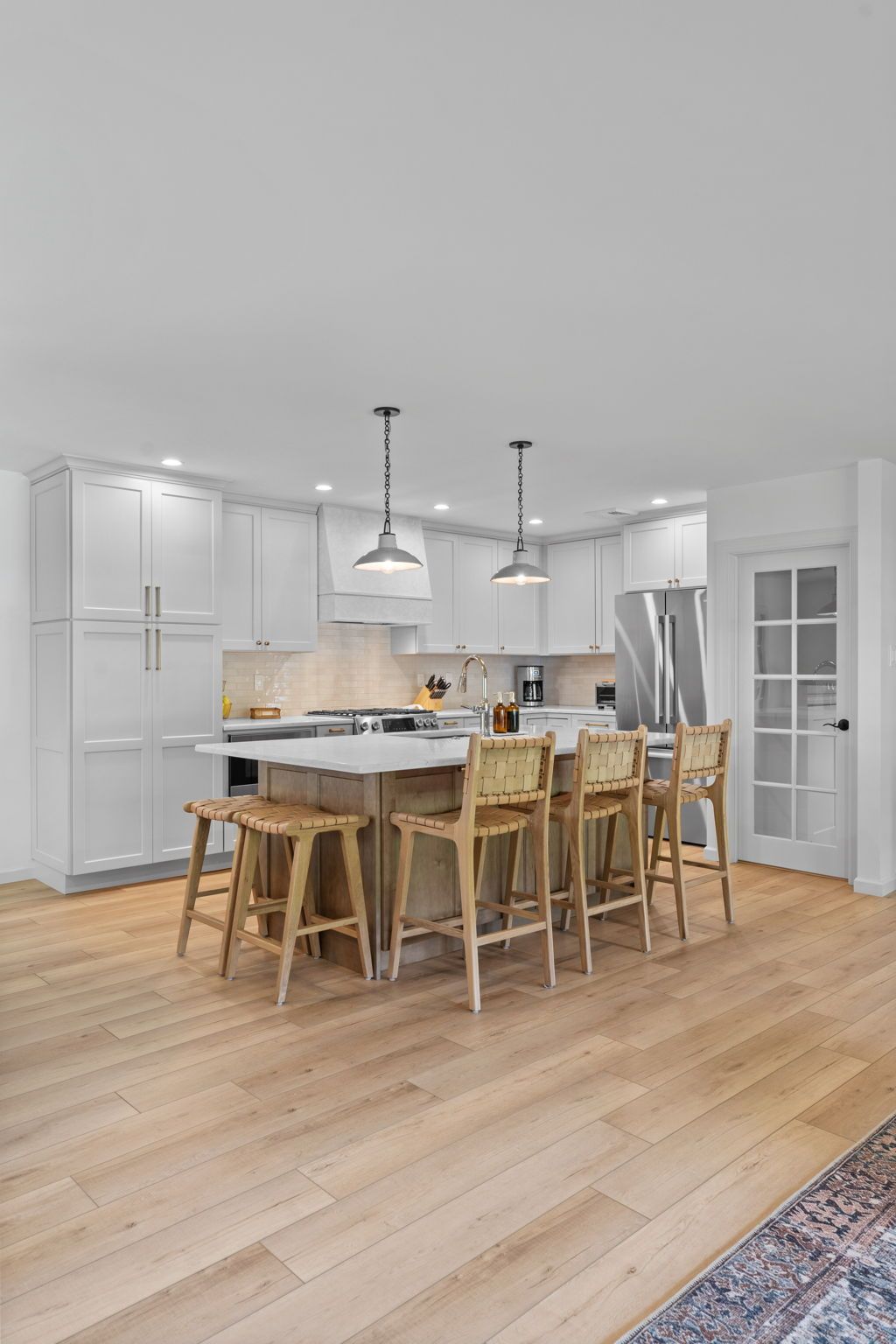 Bright modern kitchen with island, wooden stools, pendant lights, and light wood floors In Bucks County PA