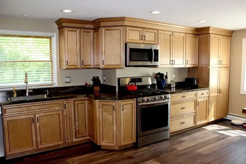 Bright kitchen with light wood cabinets, black countertops, stainless stove, and a window over the sink In Bucks Country PA