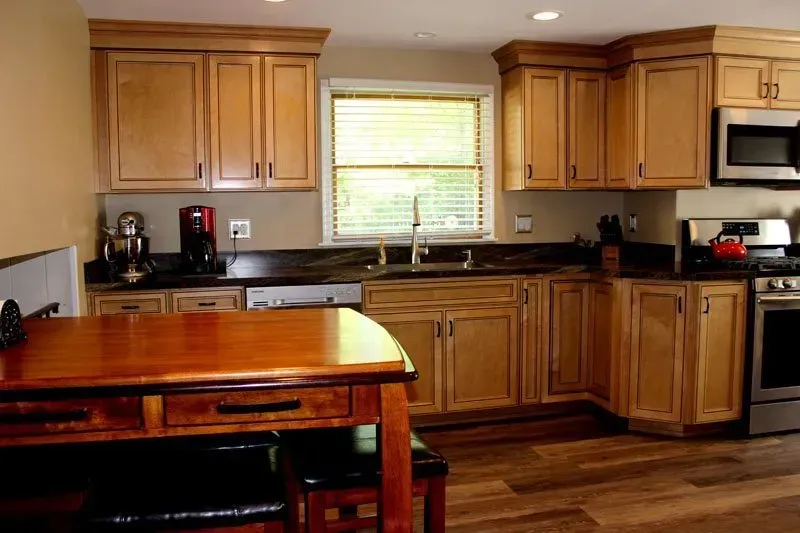 Wooden kitchen with cabinets, black countertops, center island, and a window above the sink  In Bucks County PA