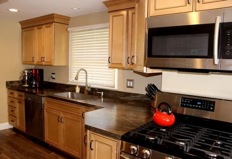 Modern kitchen with wooden cabinets, dark countertops, stainless appliances, and a red kettle on the stove  In Bucks County PA