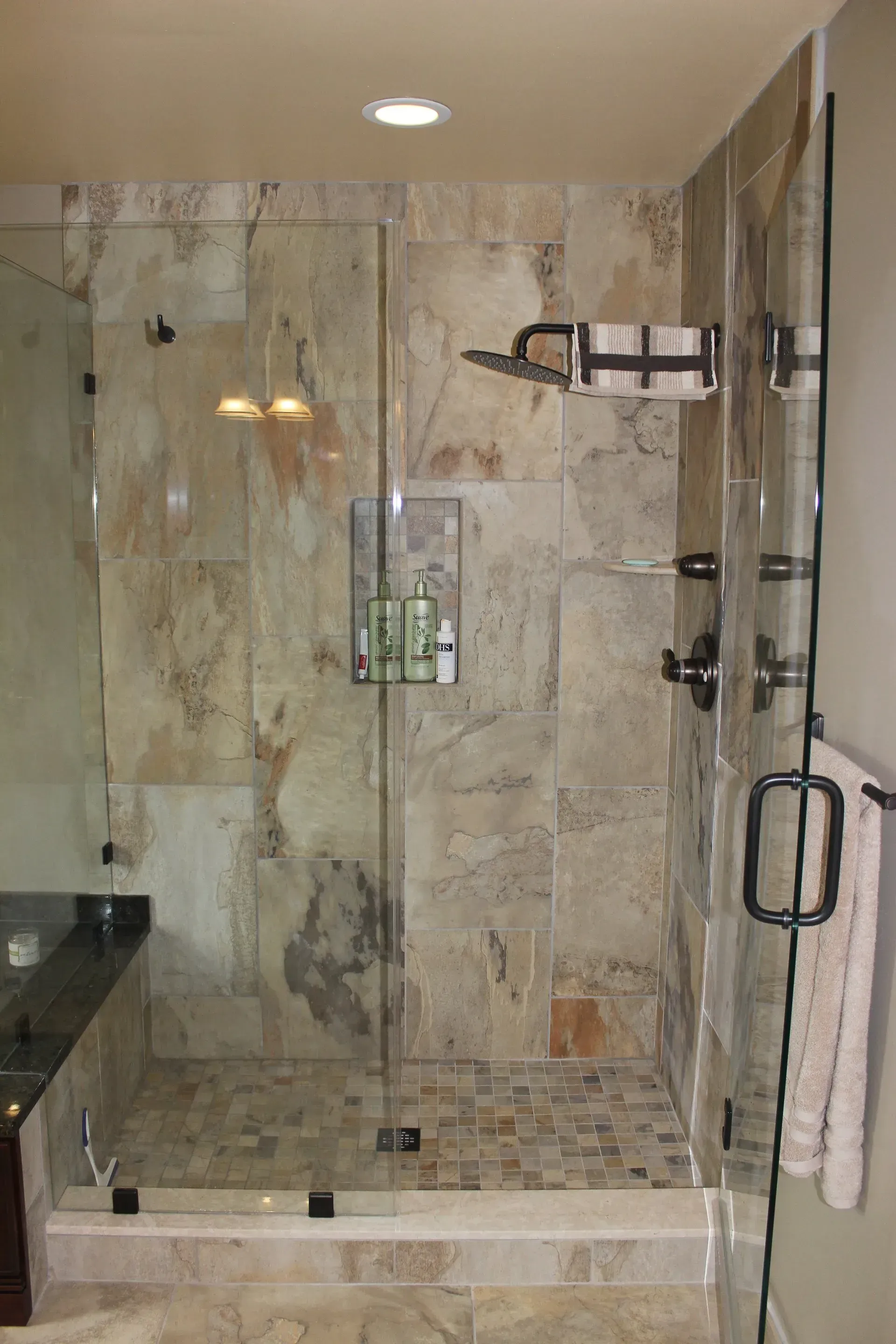 Modern tiled walk-in shower with glass enclosure, chrome fixtures, bench, and towel bar In Bucks County PA