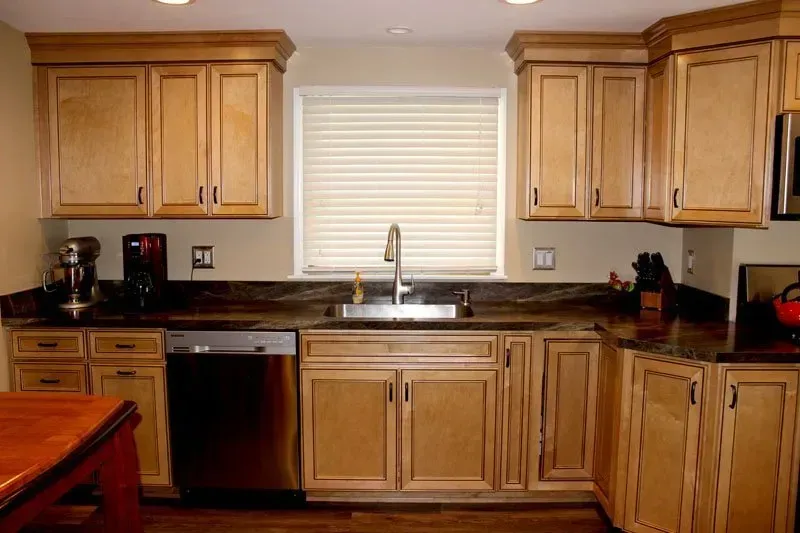 Kitchen with light wood cabinets, black countertops, stainless sink and dishwasher, and a window above the sink  In Bucks County PA