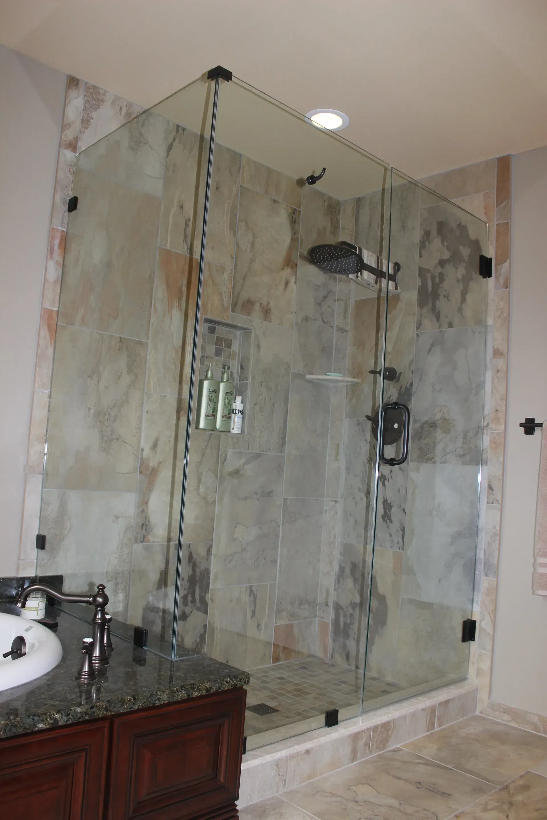 Glass-enclosed walk-in shower with marble tile, built-in shelf, and dark shower fixtures In Bucks County PA