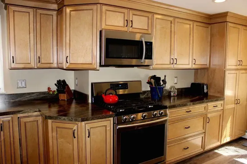 Modern kitchen with wooden cabinets, stainless stove and microwave, dark granite counters, and red cookware on the stove  In Bucks County PA