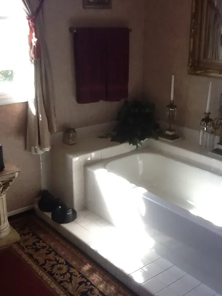 Sunlit bathroom with a white tiled bathtub, window curtains, and a candle on the ledge In Bucks County PA