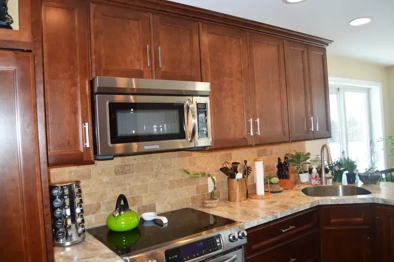 Modern kitchen with dark wood cabinets, stainless microwave, beige tile backsplash, and granite countertop In Bucks County PA