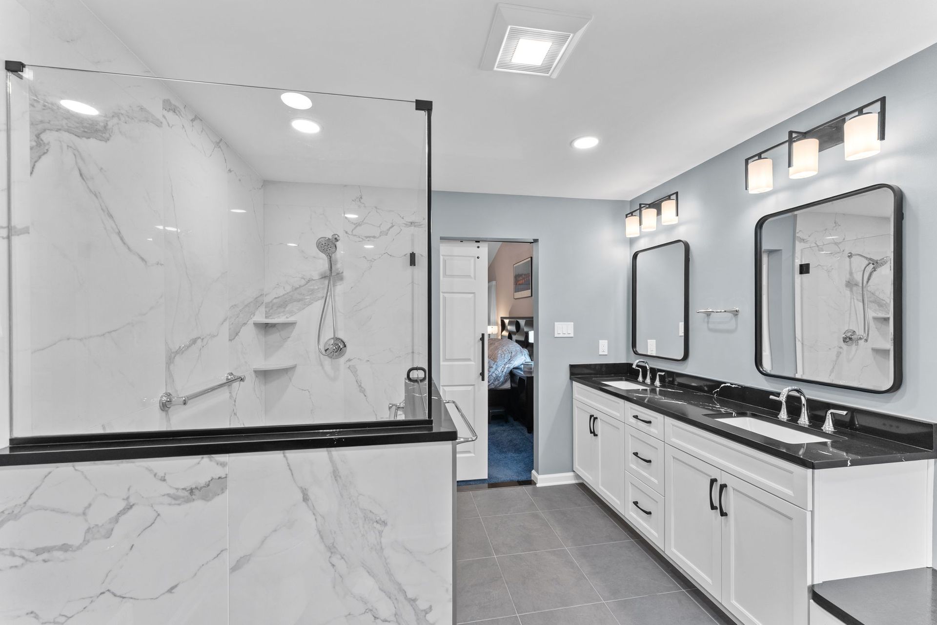 Bright modern bathroom with marble-tiled shower, black countertops, and white cabinets In Bucks County PA