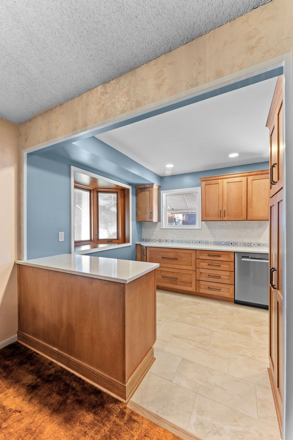 Open kitchen with wood cabinets, light counters, and a breakfast bar in a beige and blue interior In Bucks County PA