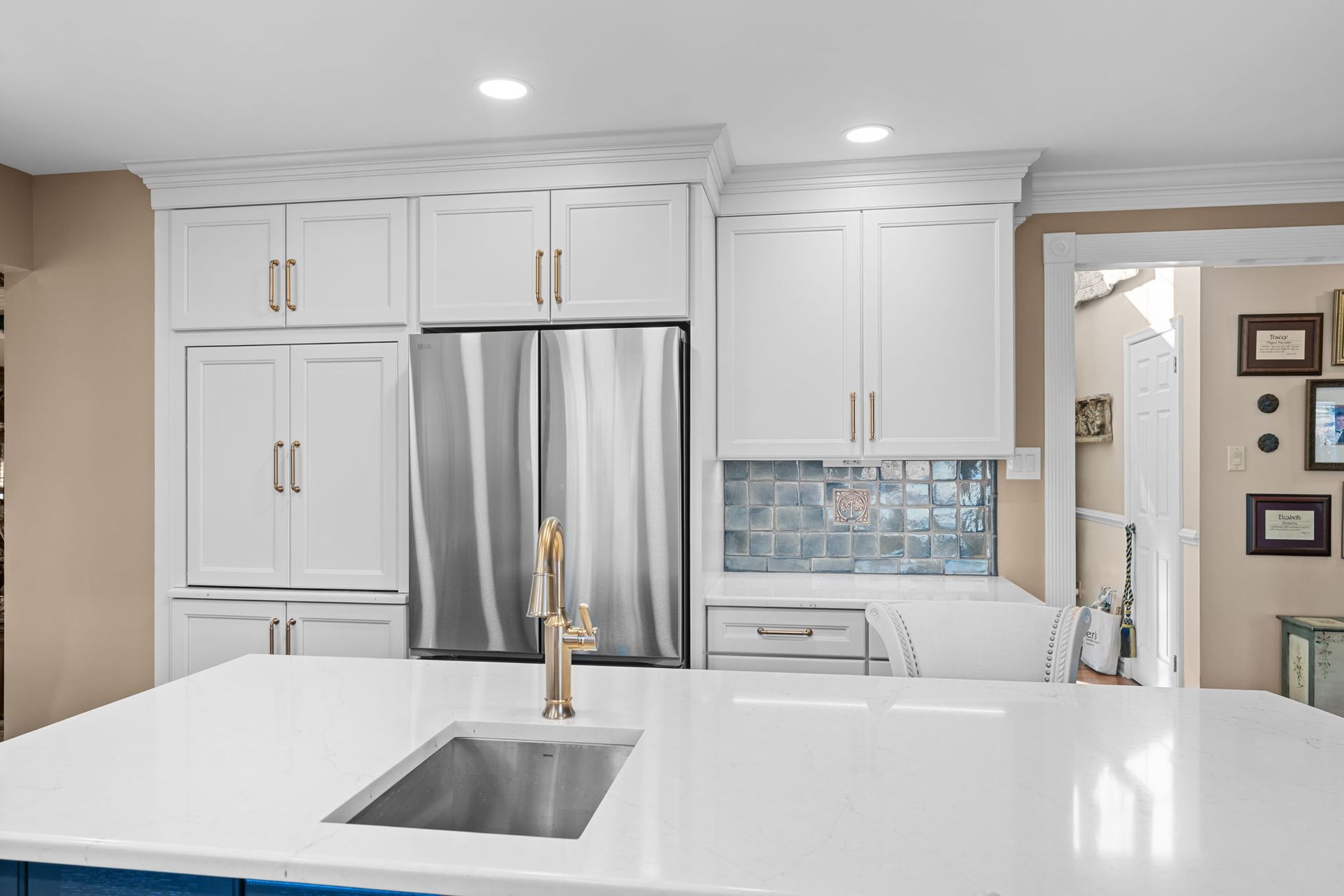 Modern white kitchen with stainless steel fridge, large island, and bright recessed lighting  In Bucks County PA