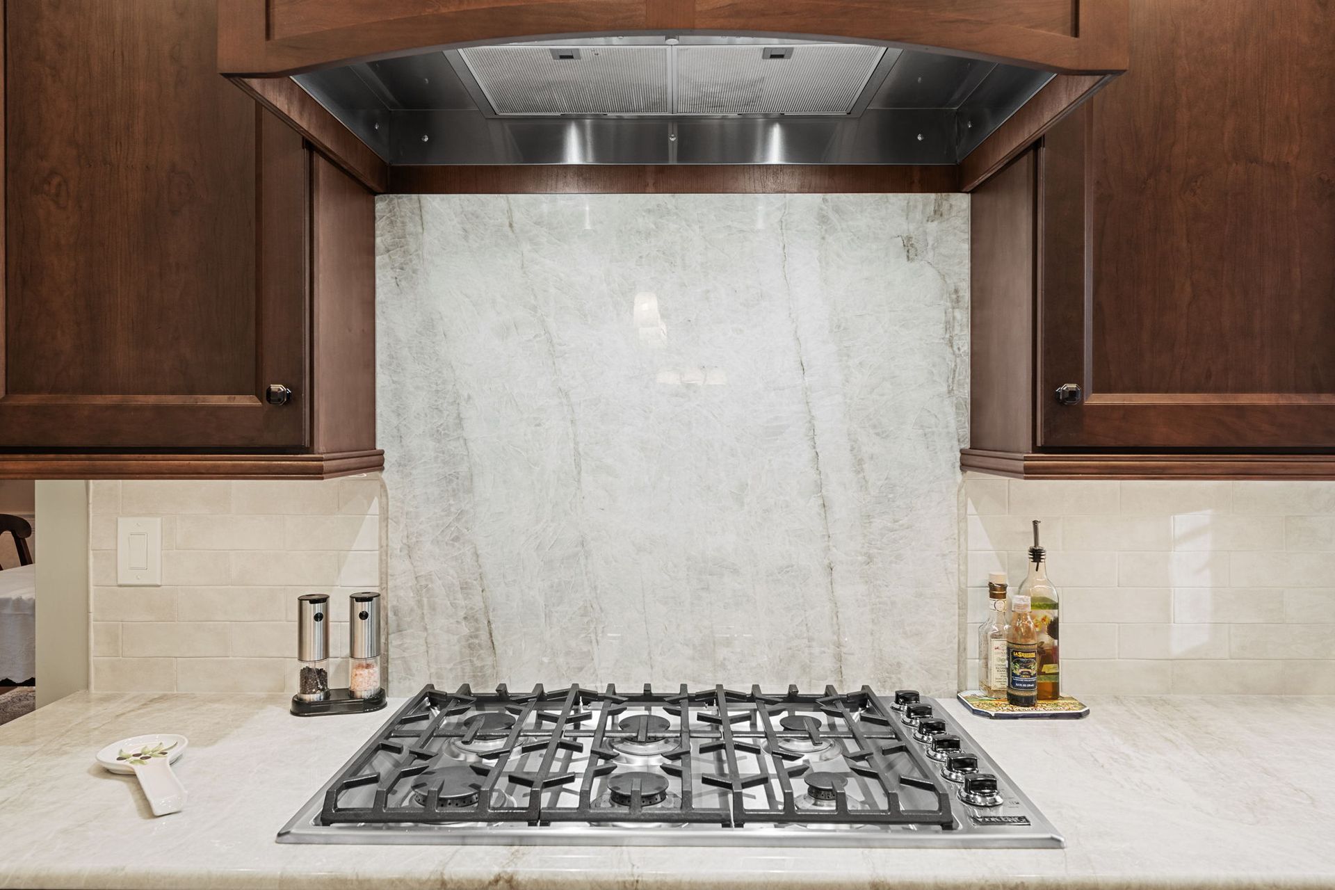 Modern kitchen stove with stainless hood, marble backsplash, and dark wood cabinets In Bucks Country PA