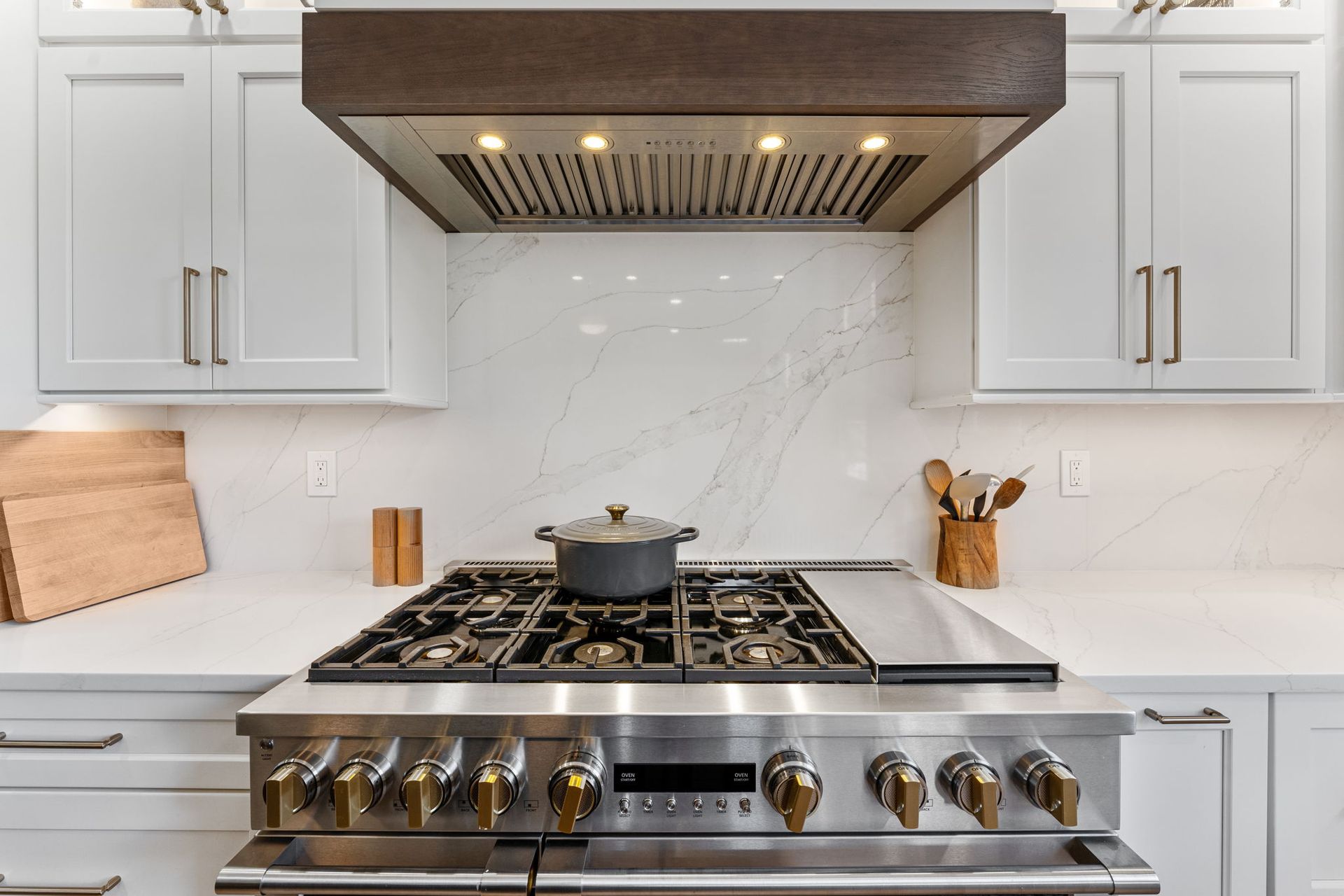 Modern white kitchen with stainless steel gas range and hood, marble backsplash, and white cabinets In Bucks Country PA