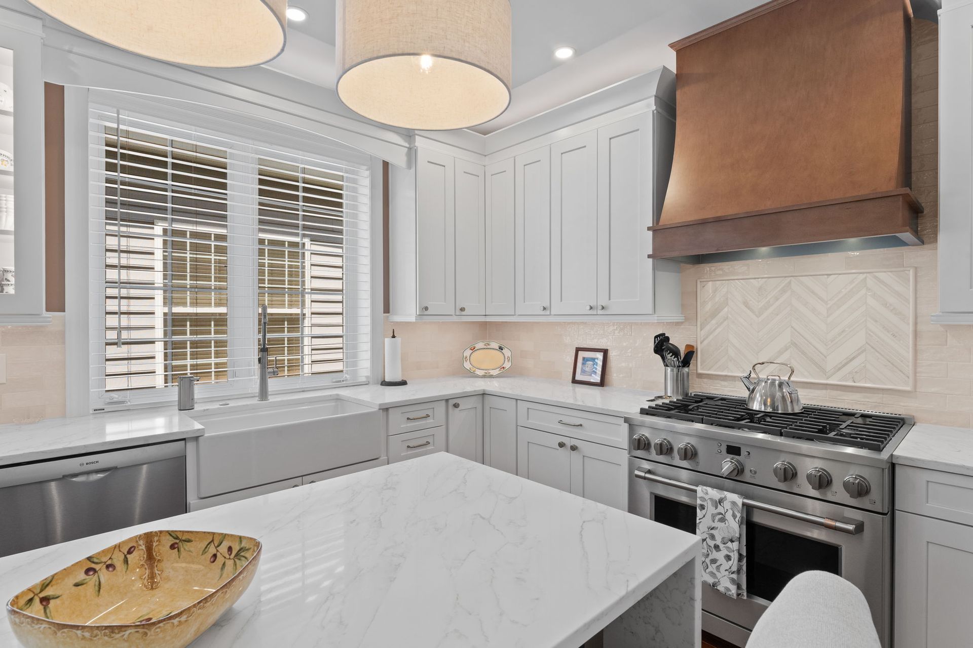 Bright white kitchen with island, gray cabinets, copper range hood, and large windows with shutters In Bucks County PA
