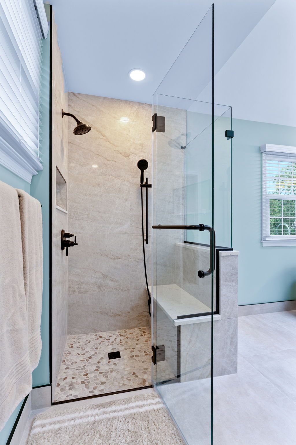 Glass-enclosed walk-in shower with marble tile, black fixtures, and a handheld showerhead In Bucks County PA