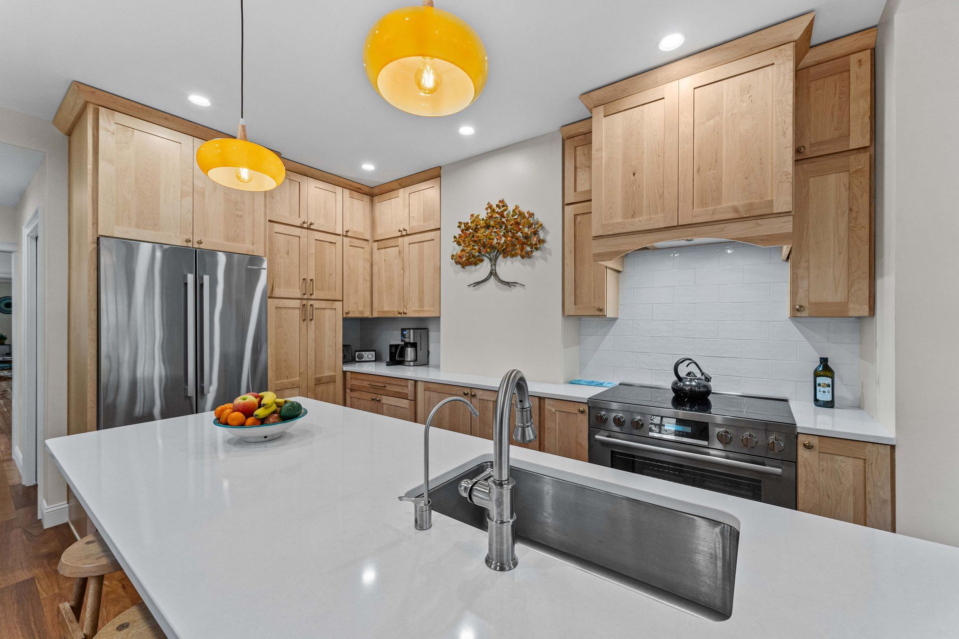 Bright modern kitchen with white island, stainless steel appliances, wood cabinets, and yellow pendant lights In Bucks County PA