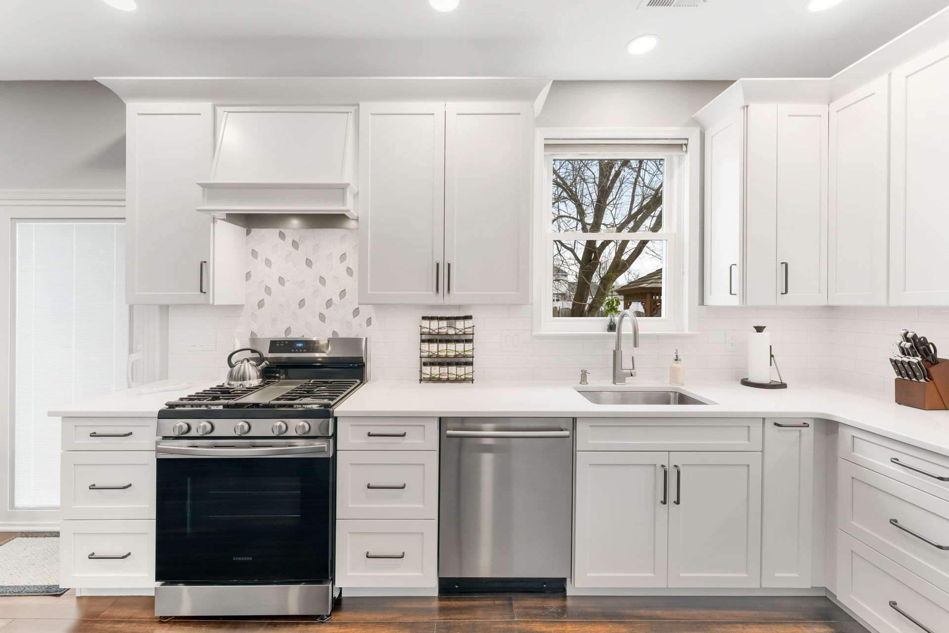Bright white modern kitchen with stainless steel appliances, island seating, and a window over the sink  In Bucks County PA