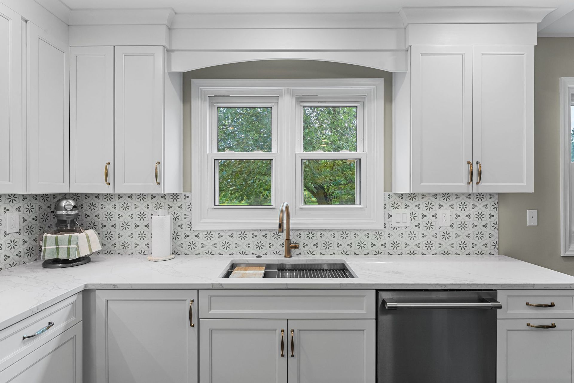 Bright white kitchen with farmhouse sink, mosaic backsplash, and window over the countertop In Bucks County PA