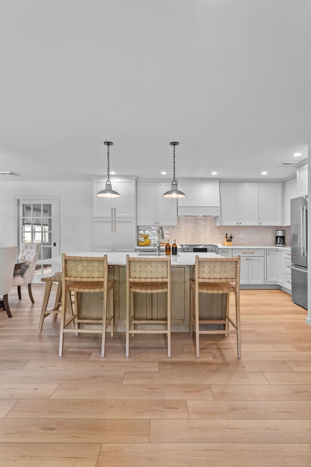 Bright modern kitchen with a white island, wooden stools, pendant lights, and light wood flooring In Bucks County PA