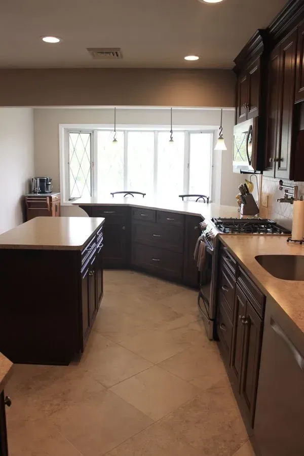 Modern kitchen with dark cabinets, beige countertops, island, and large bright windows  In Bucks County PA