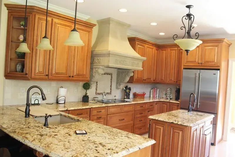Modern kitchen with granite island, wood cabinets, stainless steel fridge, and pendant lights In Bucks Country PA