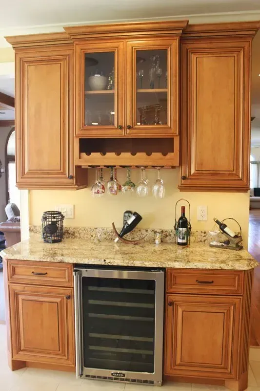 Wooden kitchen cabinets, granite countertop, wine cooler, and glass-front hutch on a beige wall In Bucks County PA