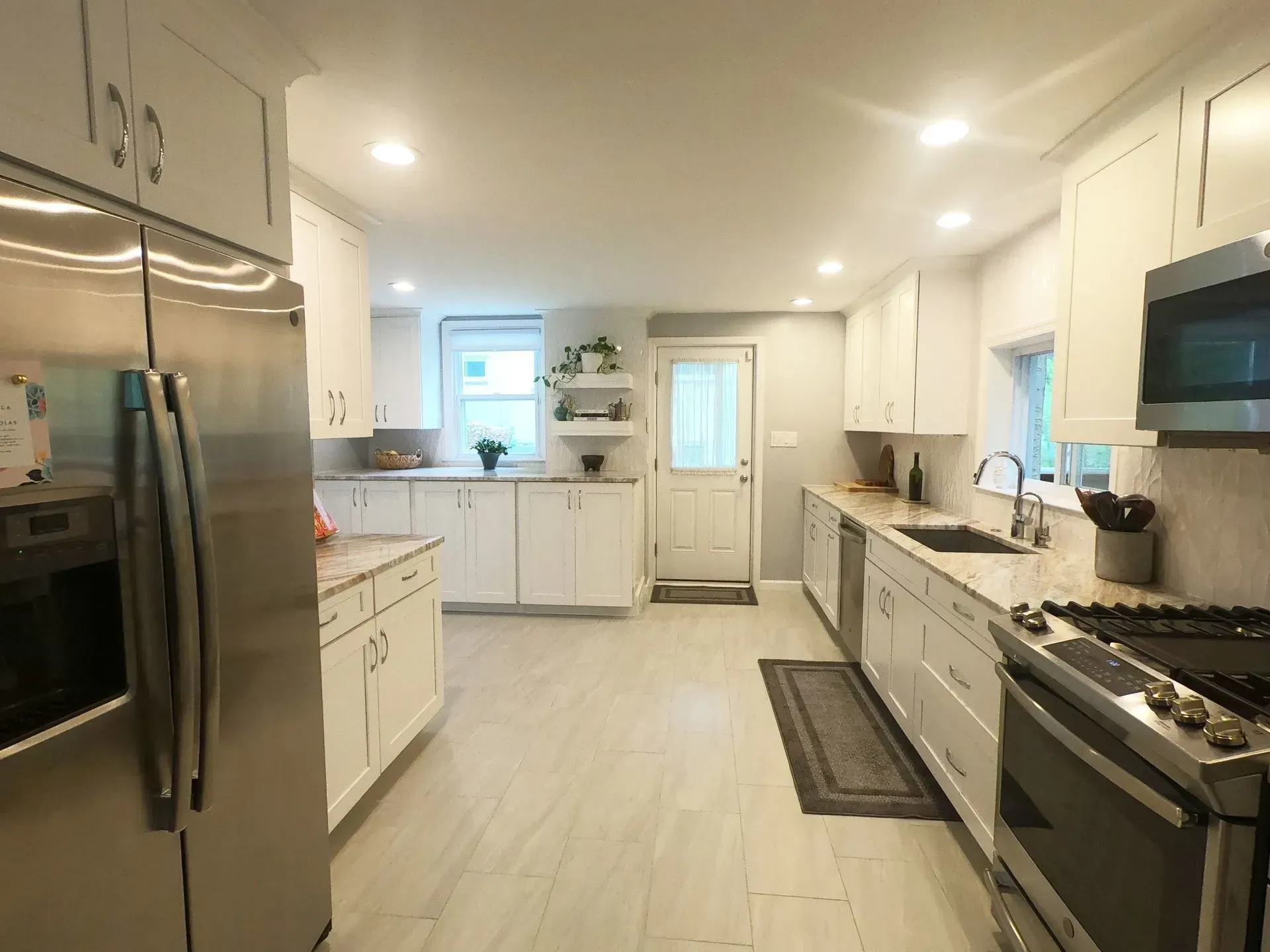 Bright modern white kitchen with stainless steel appliances, island, and window over sink In Bucks Country PA