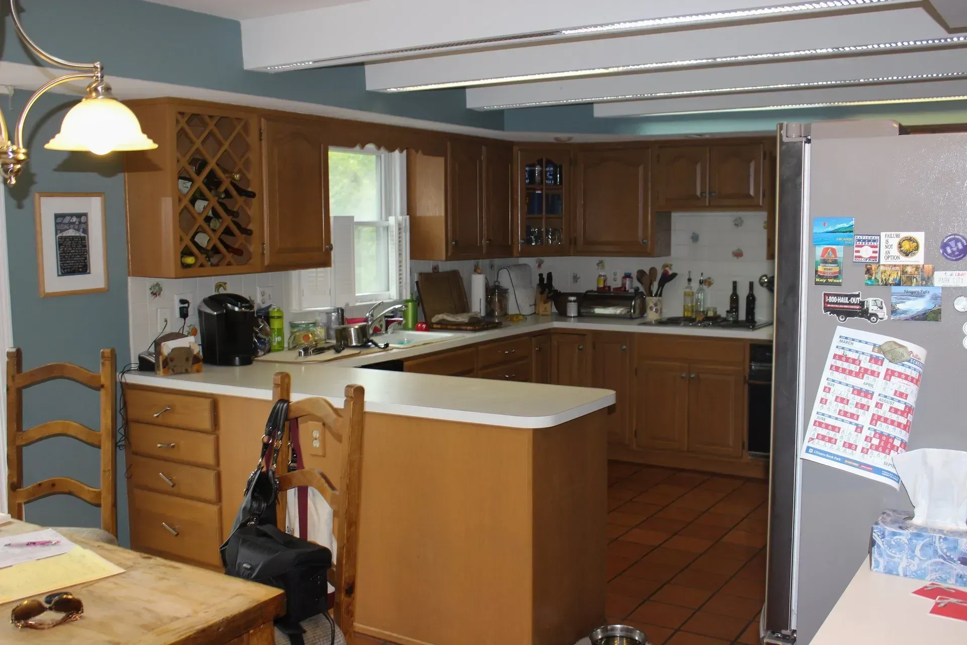 Bright kitchen with wood cabinets, white island, dining chair, and a refrigerator covered in magnets  In Bucks County PA