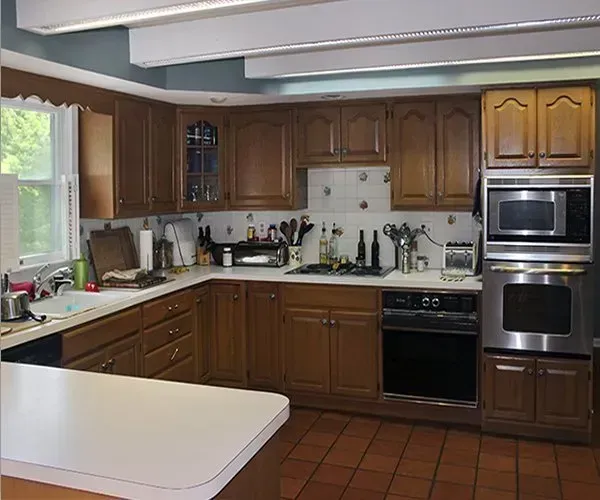 Brown wood kitchen with white countertops, tiled floor, and built-in oven beside a window  In Bucks County PA
