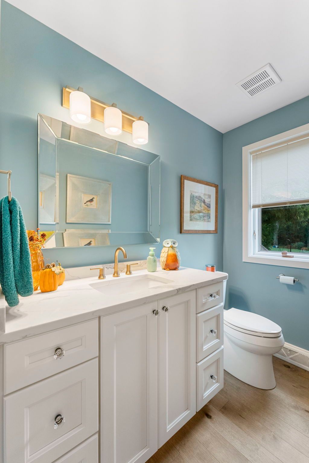 Bright blue bathroom with white vanity, mirror lights, and a window beside the toilet  In Bucks County PA