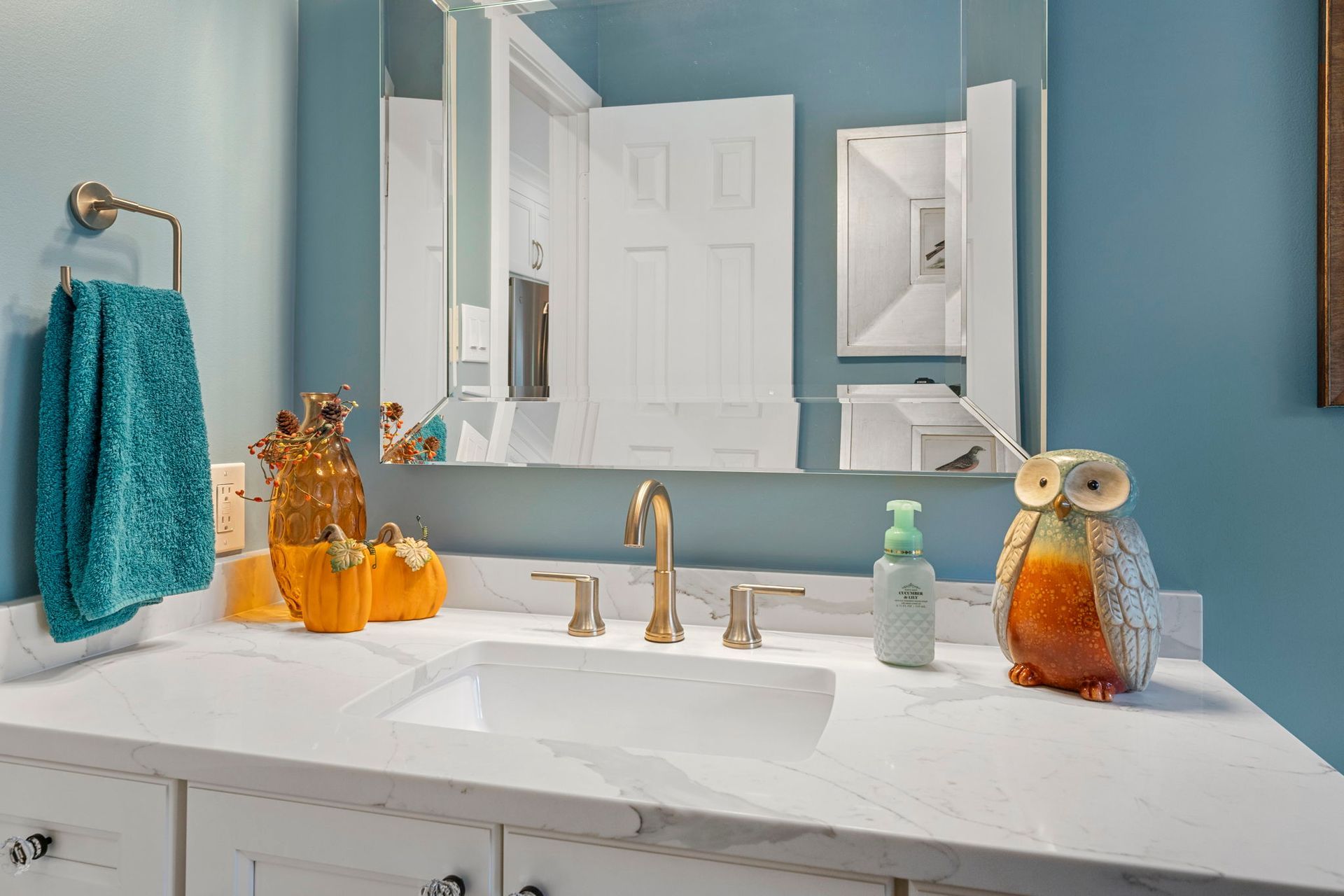 Blue bathroom vanity with mirror, white countertop, and owl decor on the sink area  In Bucks County PA