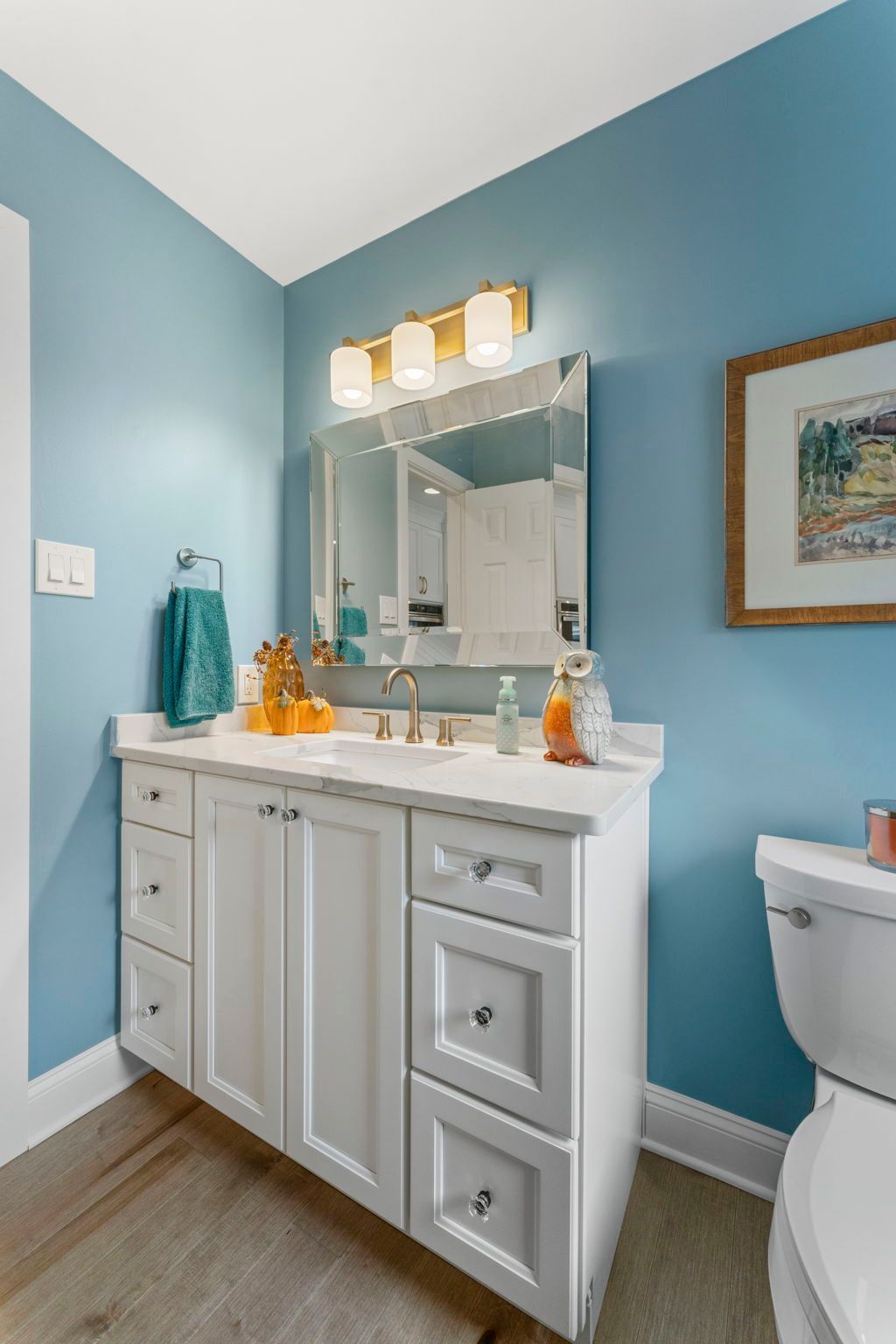 Blue bathroom with white vanity, mirror lights, and a toilet on the right  In Bucks County PA