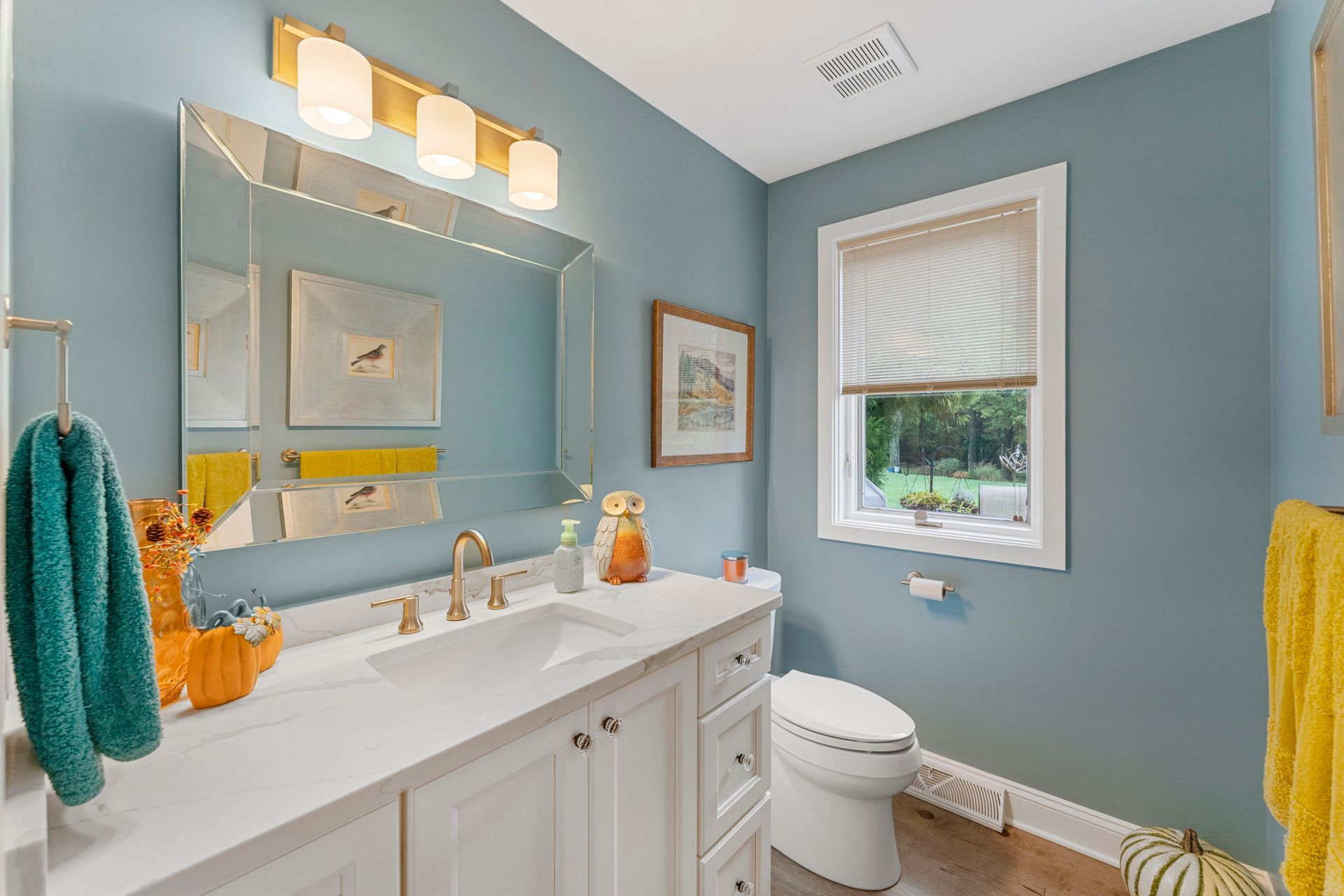 Light blue bathroom with white vanity, mirror, window, and colorful towels  In Bucks County PA