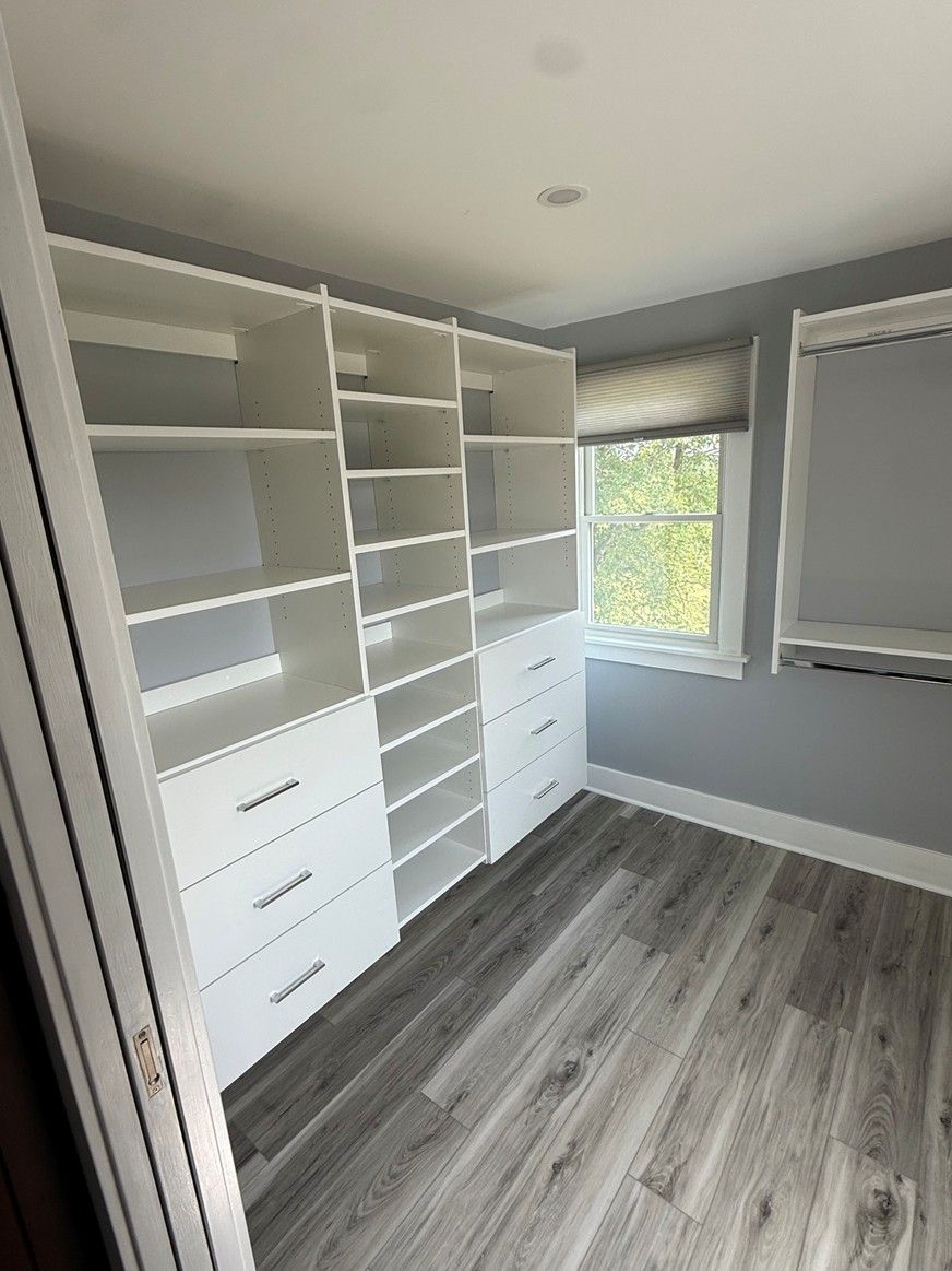 Empty walk-in closet with white shelving and drawers, gray walls, and wood-look flooring  In Bucks County PA