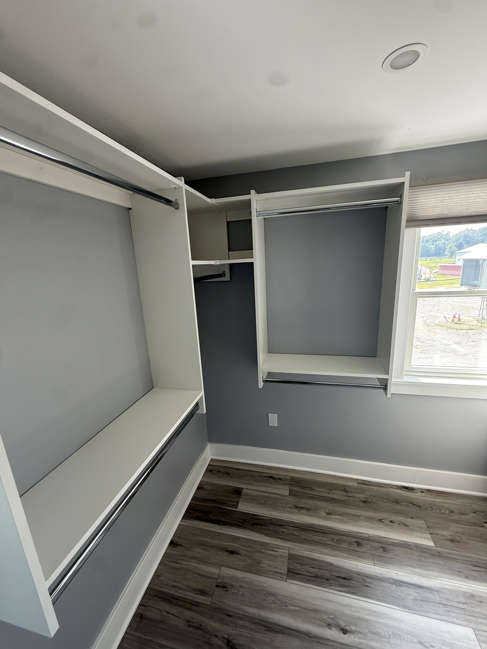 Empty closet with gray walls, built-in shelving, and wood-look flooring near a window In Bucks County PA