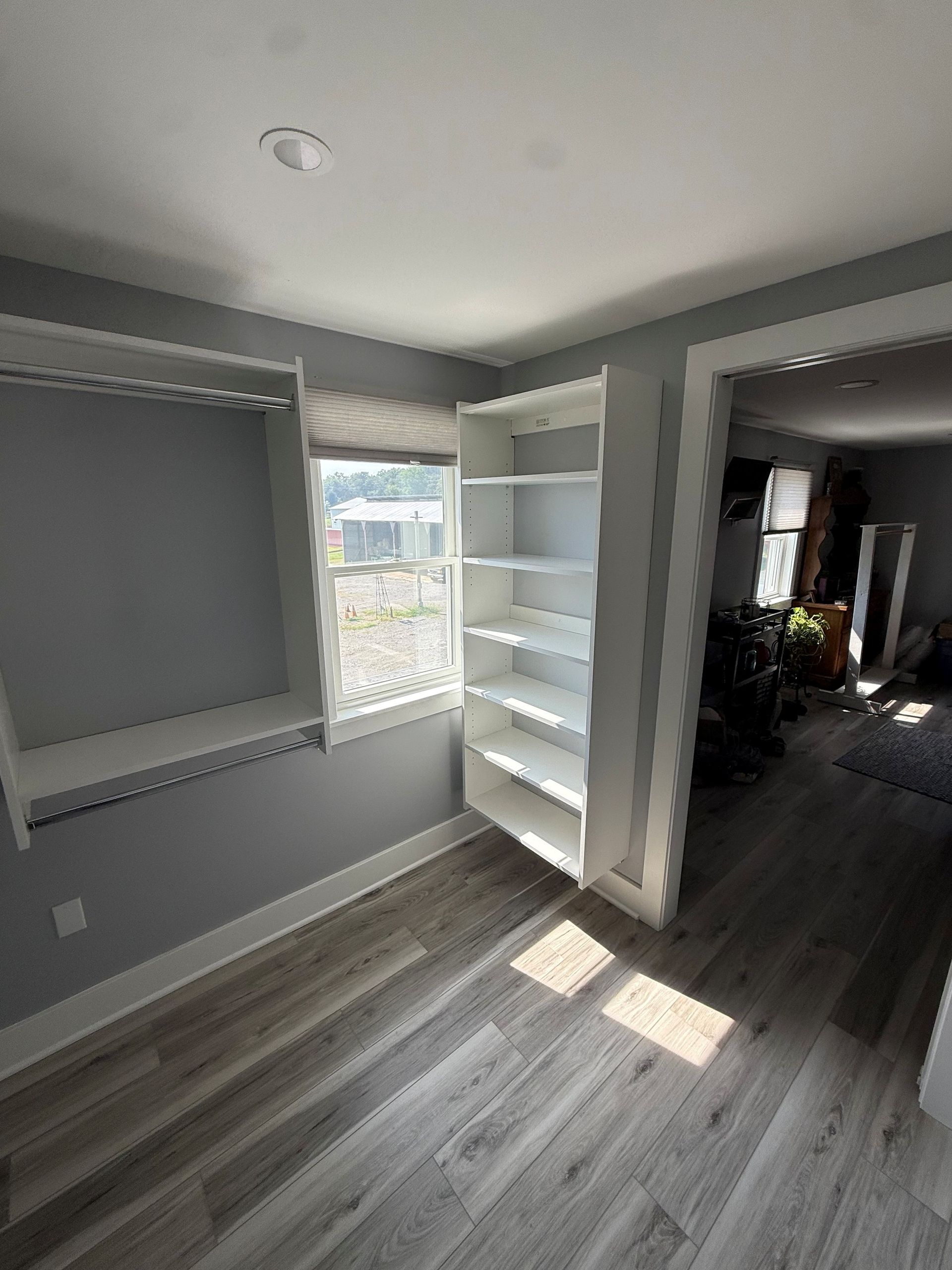 Empty gray bedroom with window, white shelving, and sunlight on gray wood floor In Bucks County PA