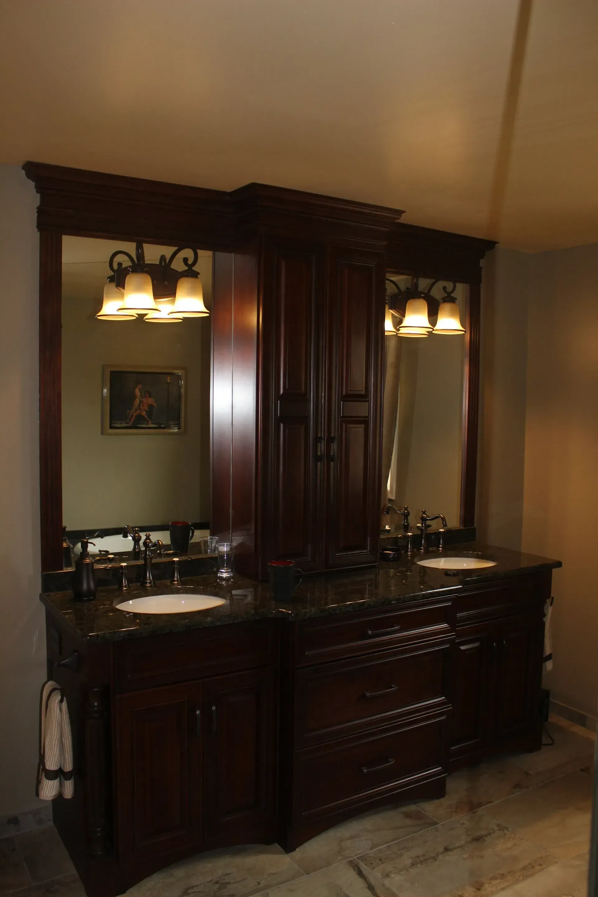 Dark wooden bathroom vanity with dual mirrors, sinks, and wall sconces against beige walls  In Bucks County PA