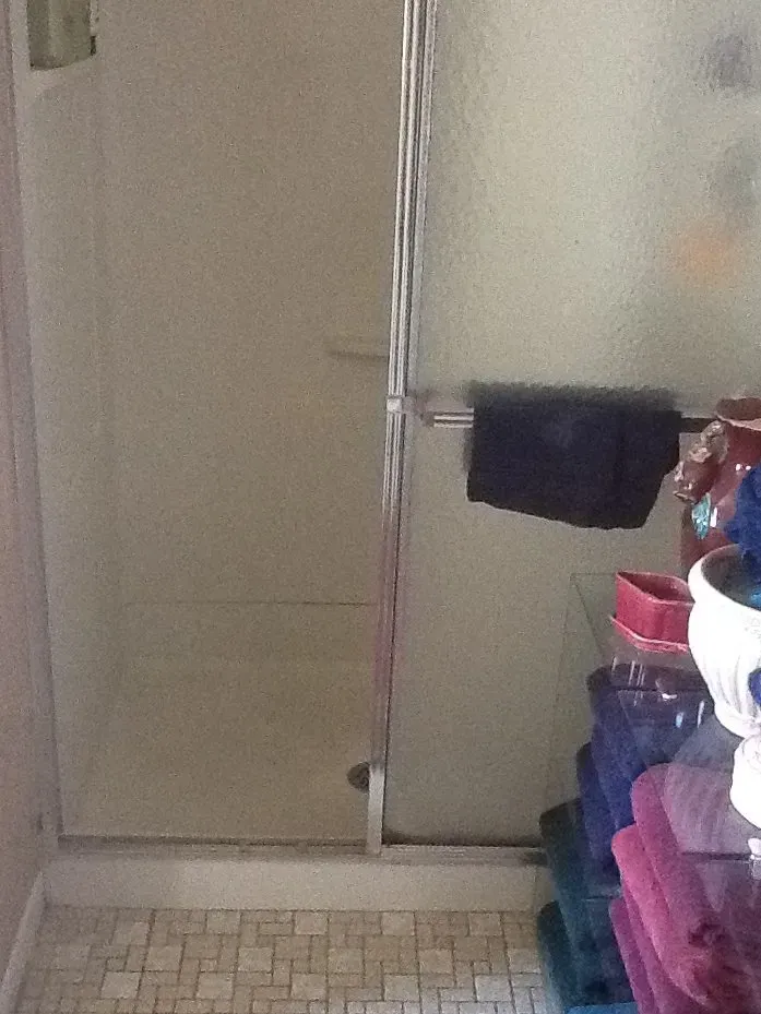 Small bathroom with tiled floor, shower door, and stacked towels and toiletries on the right  In Bucks County PA