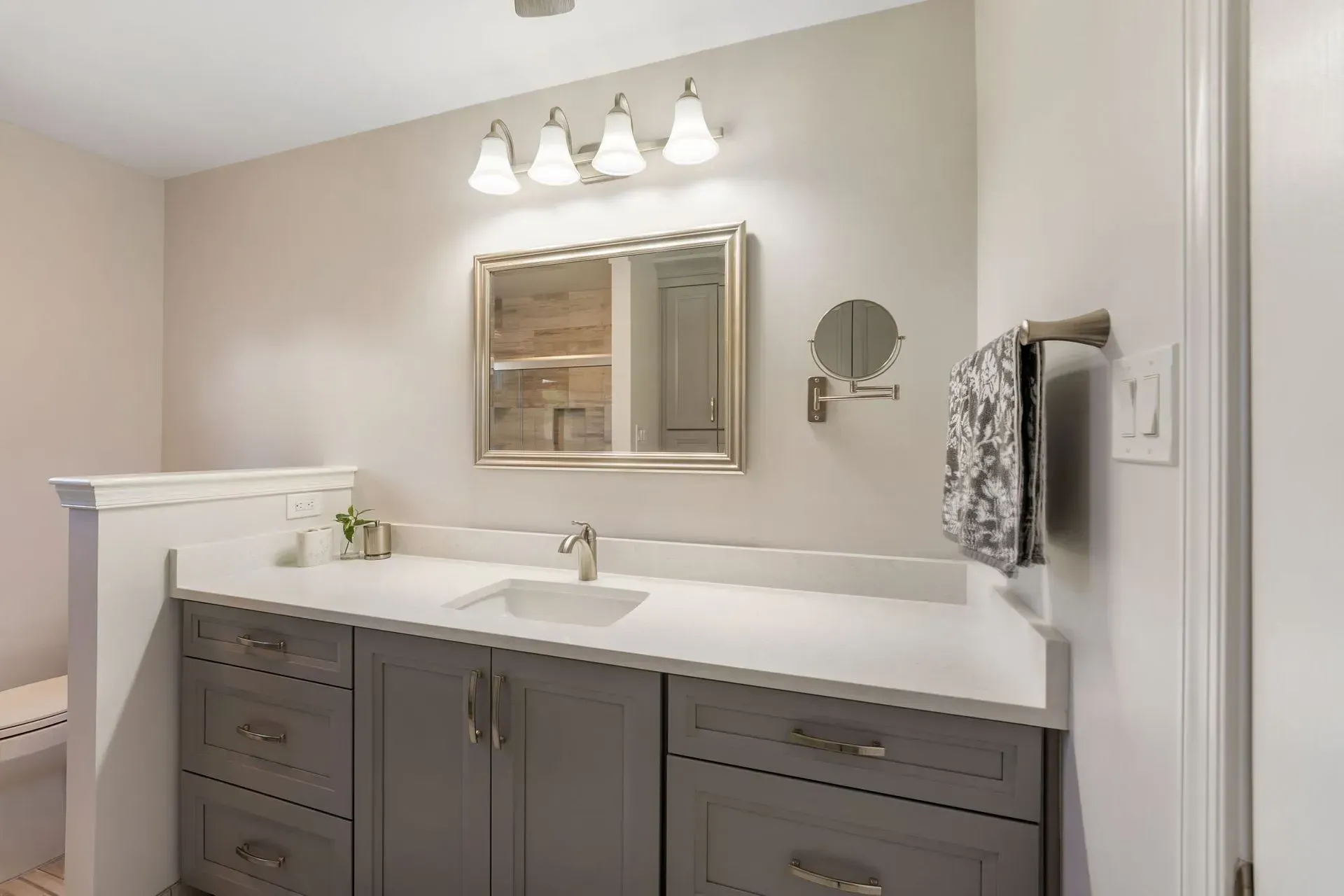 Modern bathroom vanity with gray cabinets, white countertop, mirror, and three-light wall fixture  In Bucks County PA