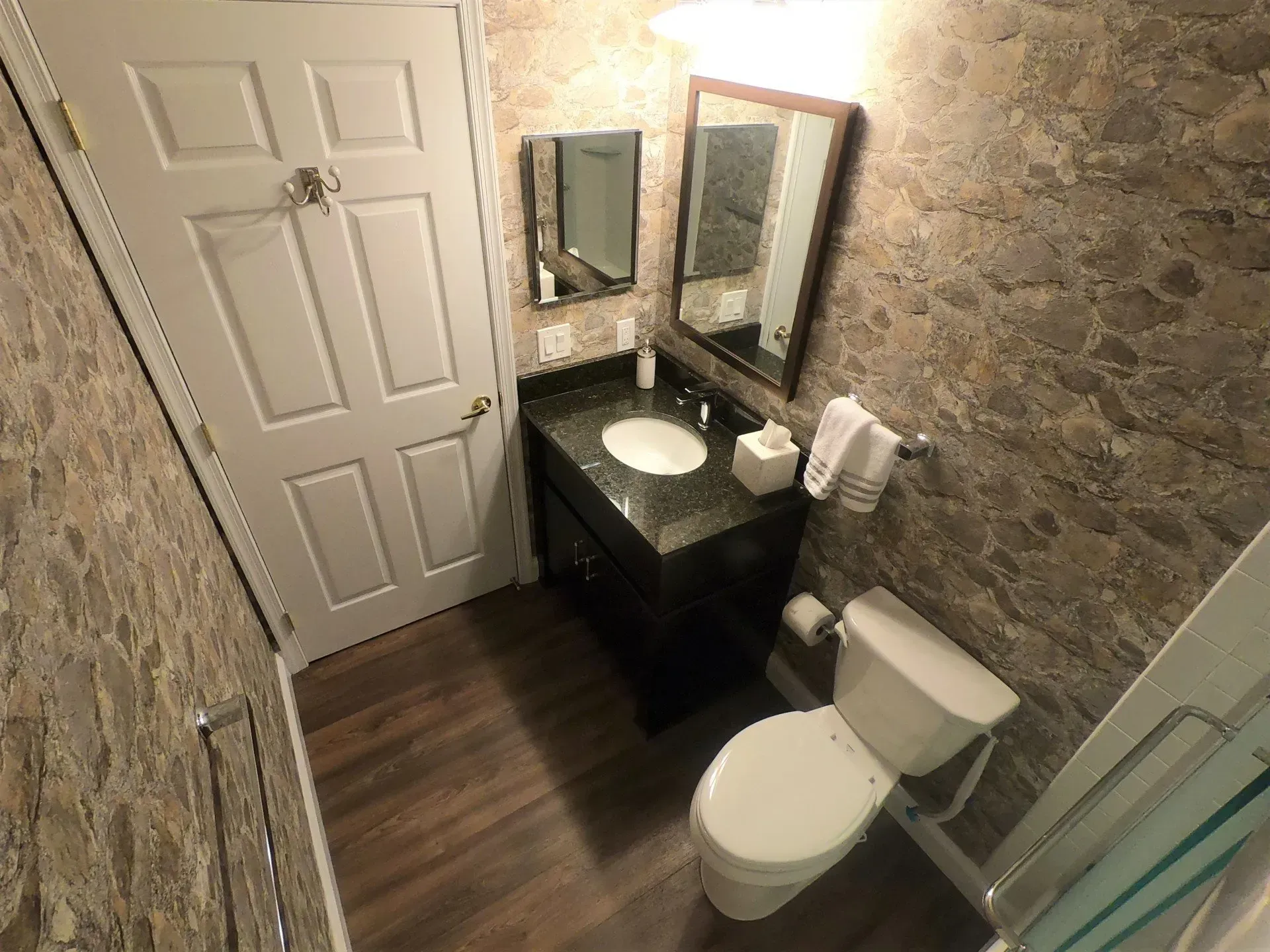 Small bathroom with stone walls, dark vanity, toilet, mirrors, and glass shower door  In Bucks County PA