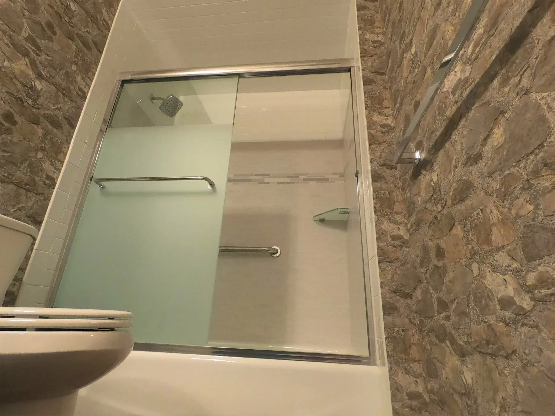 Bathroom shower with frosted glass door and marble tile walls, with a sink in the foreground  In Bucks County PA