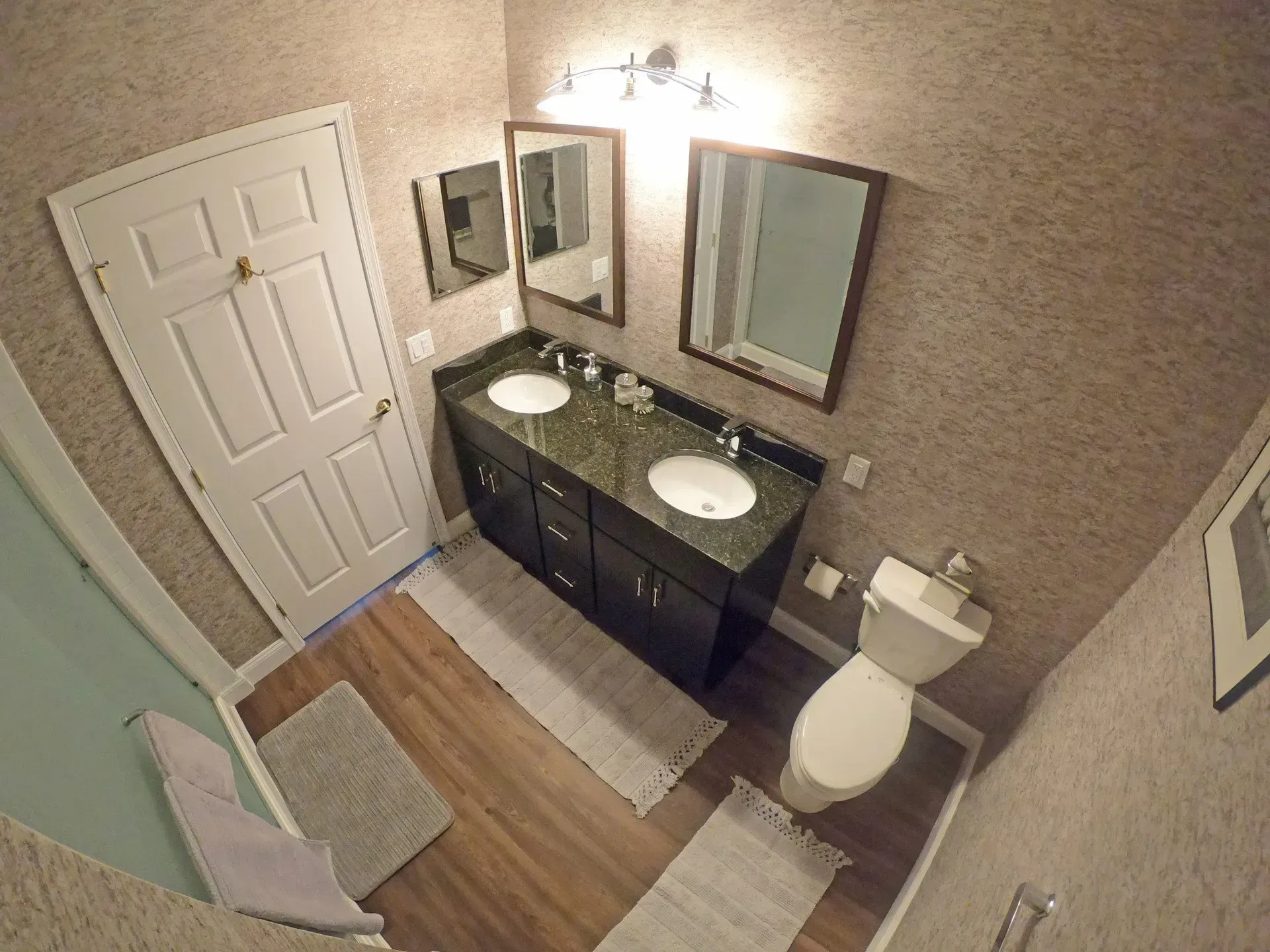 Small bathroom with double vanity, mirrors, toilet, shower curtain, and wood floor In Bucks County PA